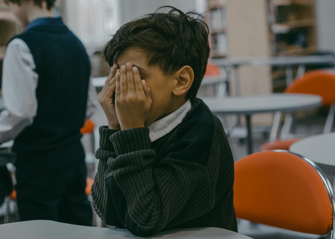 A child with hands covering face, experiencing bullying in a school setting.