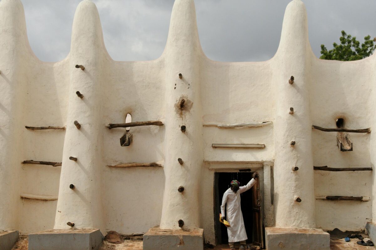 A person entering an adobe mosque with wooden architectural elements in Africa.