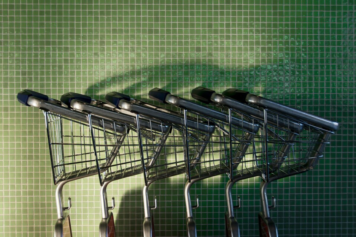 A row of neatly arranged shopping carts in front of a green tiled wall with shadows.