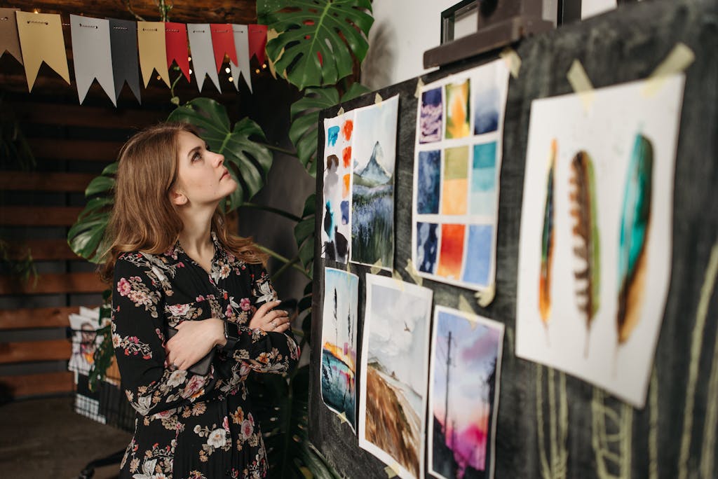 A woman in a floral dress observes art pieces on a board in her creative workshop.