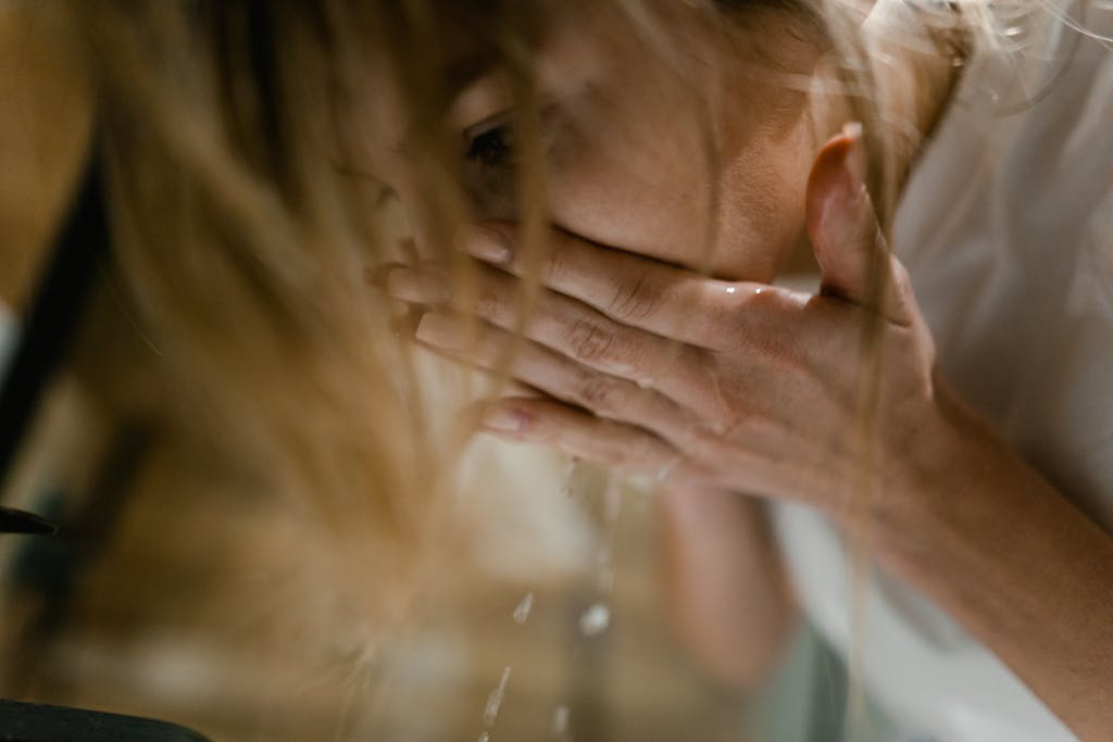 A woman splashes water on her face, emphasizing refreshing skincare routine.