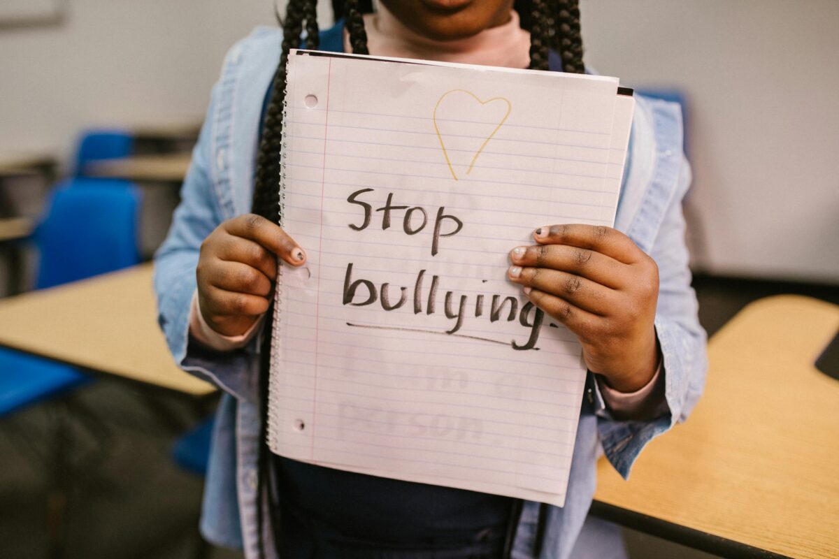 A young girl holds a "Stop Bullying" sign in a classroom setting.