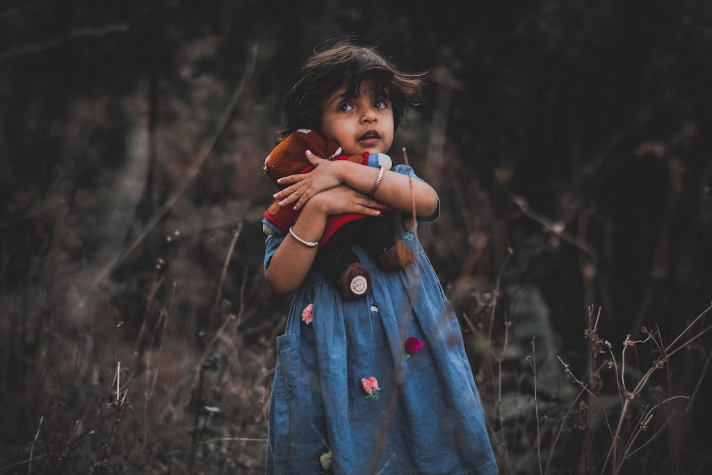 Adorable child in a blue dress holding a stuffed toy outdoors, full of innocence and charm.