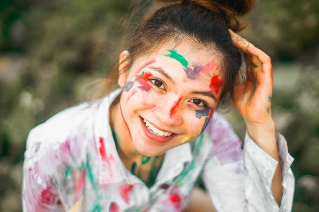 Cheerful woman outdoors with vibrant face paint and a big smile, expressing creativity and freedom.