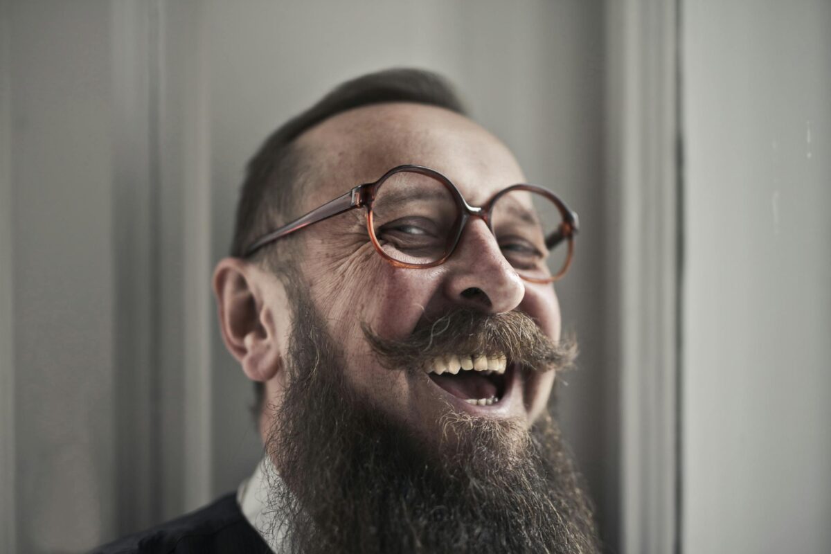 Close-up of a happy, bearded man wearing glasses laughing indoors.