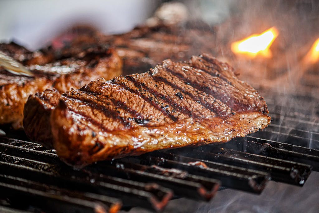 High-quality close-up of a deliciously juicy grilled steak on a barbecue grill, flames flickering in the background.