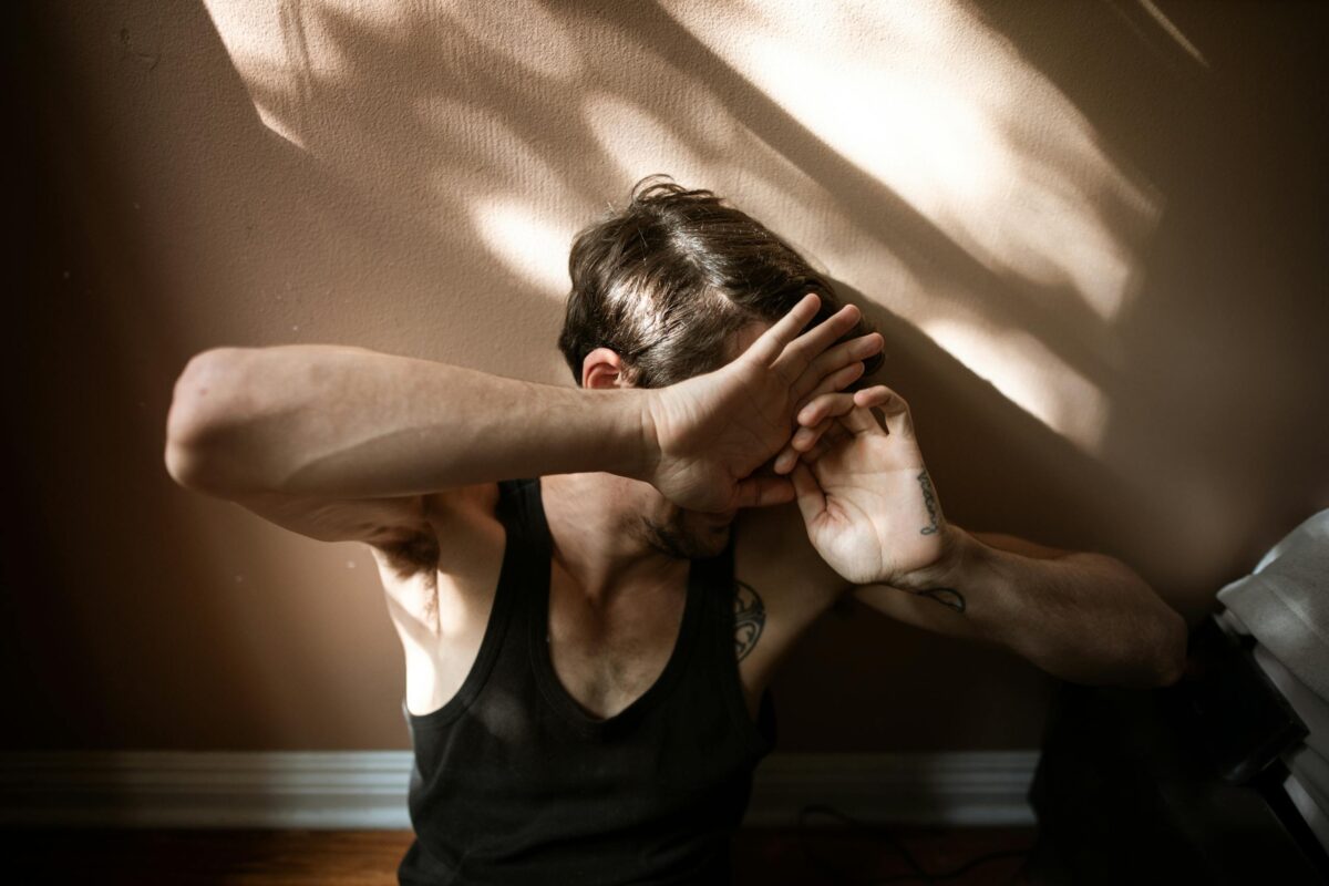 Man sitting by the wall showing expressive emotion surrounded by shadows inside a room.