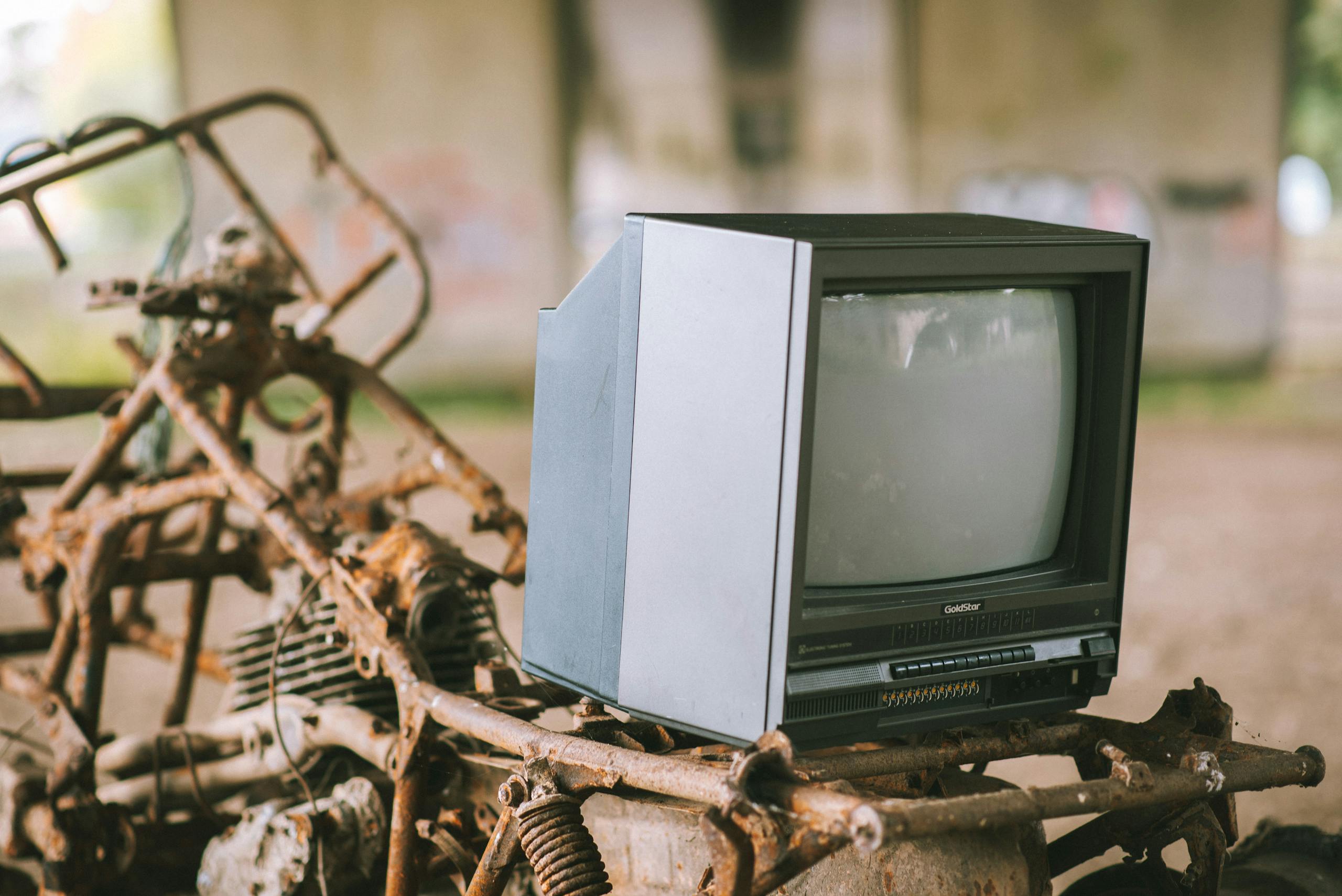 Old television set on a rusting frame under a bridge, evoking nostalgia and urban decay.